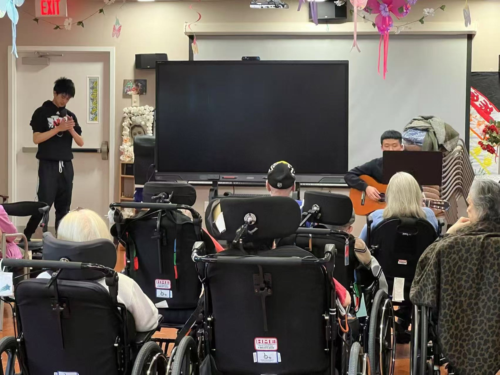 Wide view of a SEIVN performance — a student playing guitar for residents at a senior care center